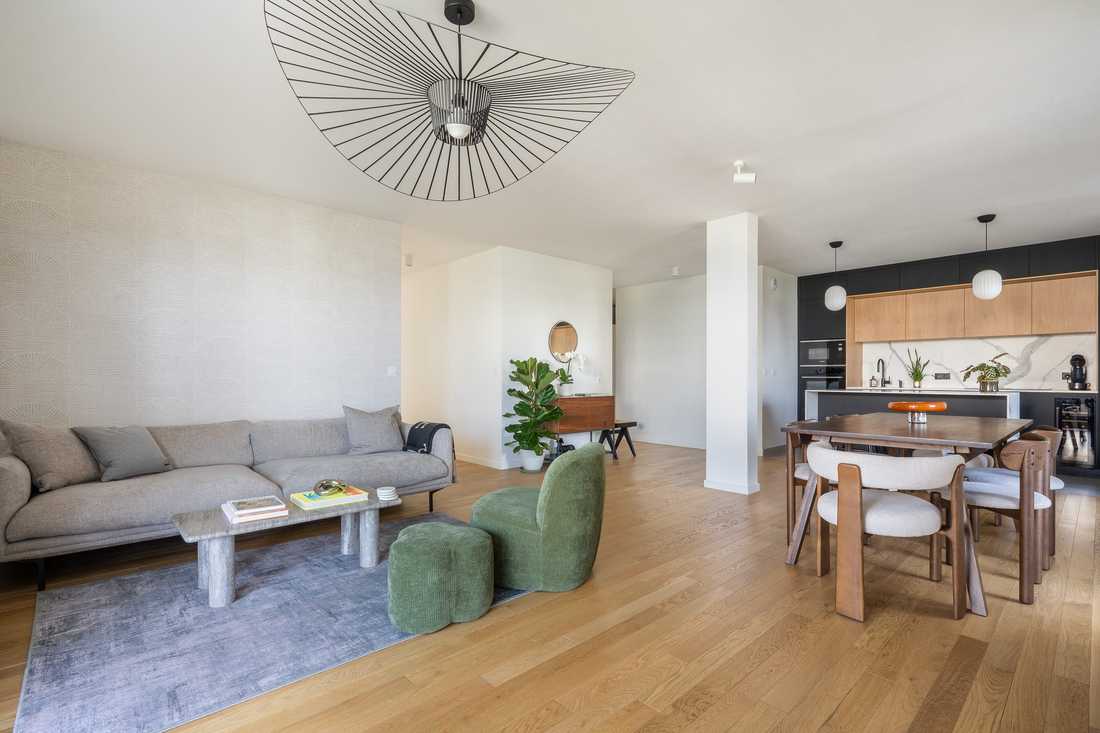 Séjour ouvert sur la salle à manger et la cuisine, avec canapé gris et fauteuil vert