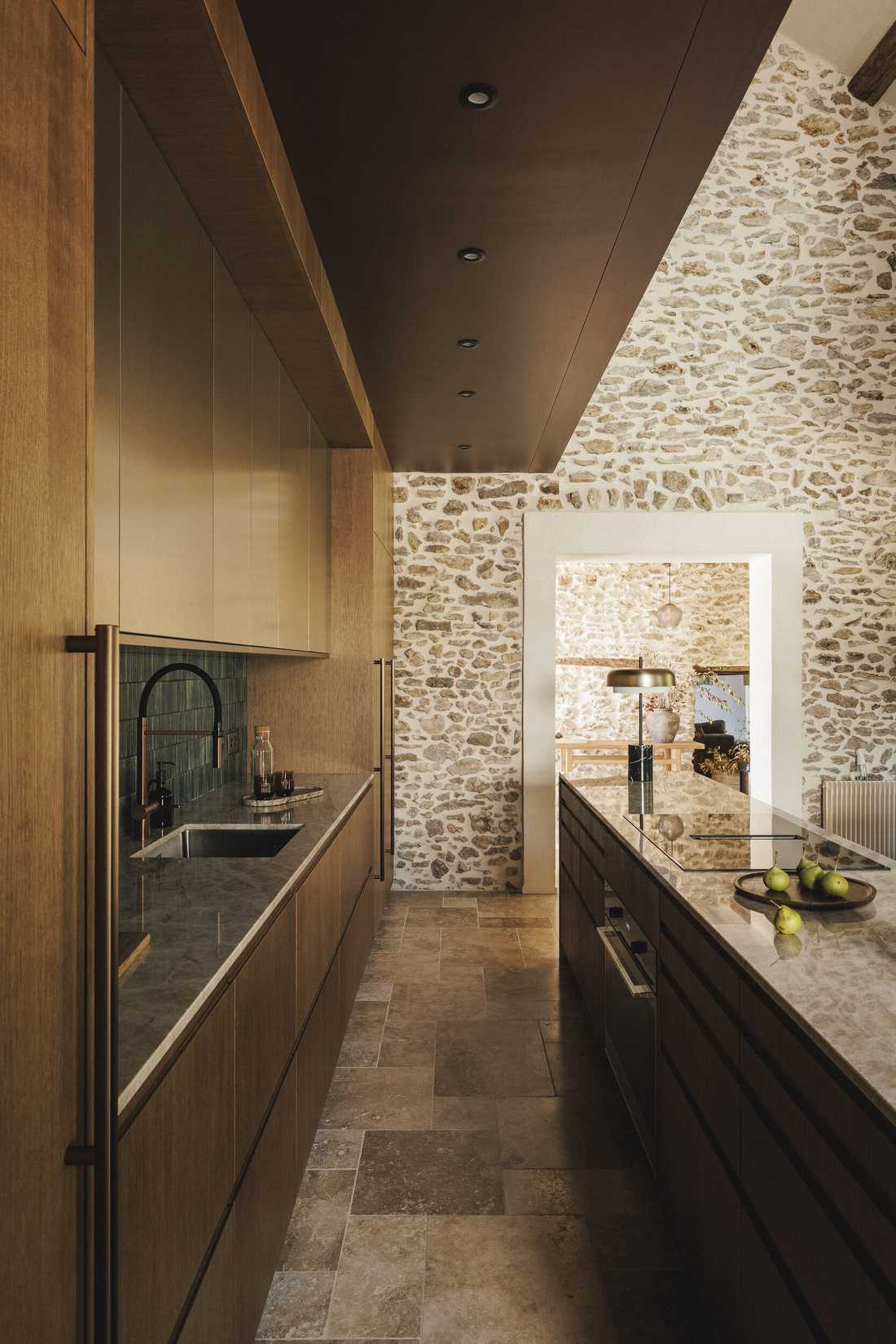 Rénovation complète d’une longère au cœur de la forêt - la cuisine en enfilade vers le mur en pierre