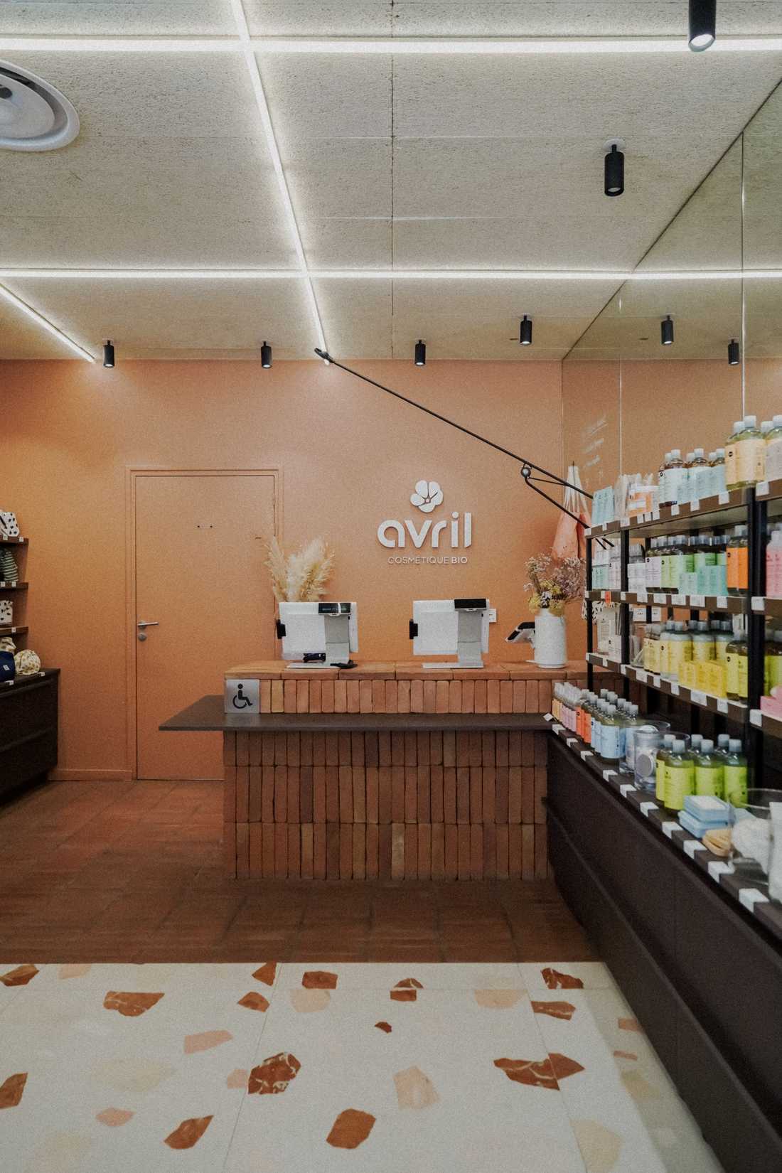 Aménagement du comptoir caisse de la boutique Avril à Antibes, enseigne sur mur enduit terracotta