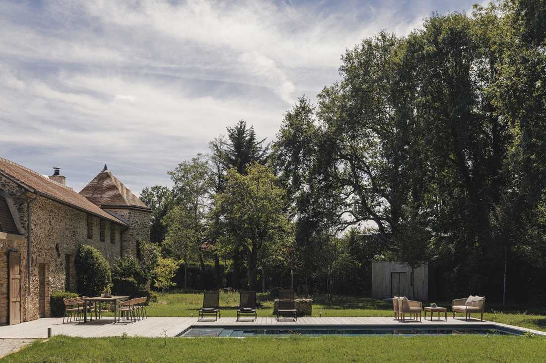 Création d’une piscine dans le jardin d’une longère - le jardin bordé de grands arbres, la piscine et la terrasse en bois