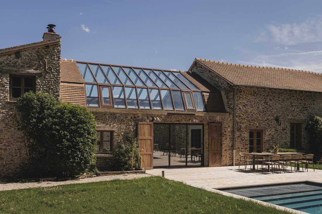 Création d’une piscine dans le jardin d’une longère - la verrière de l'ancienne grange et la table de repas sur la terrasse