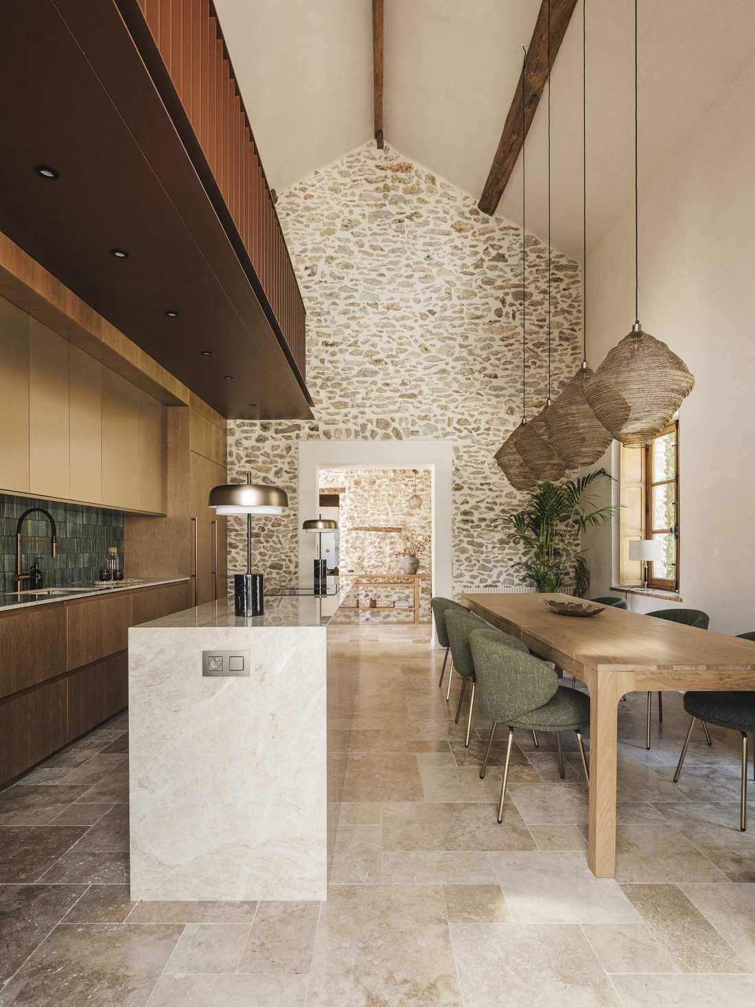 Rénovation complète d’une longère au cœur de la forêt - l'îlot de cuisine, la table en chêne et les suspensions sous le mur en pierre
